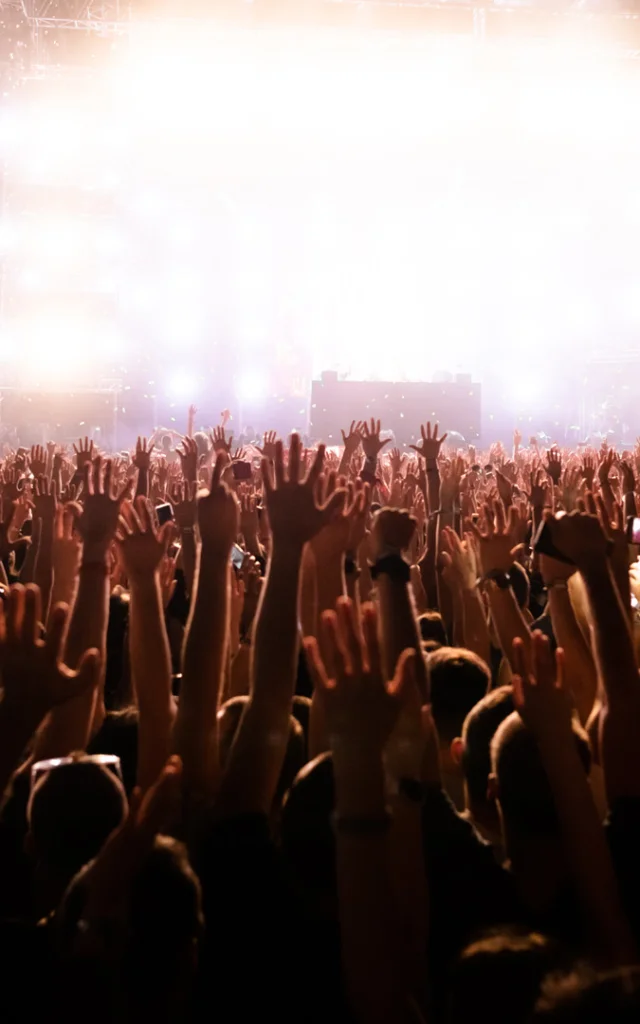 Rear view of excited people with arms raised having fun while watching confetti fireworks in front of the stage at music festival. Copy space.